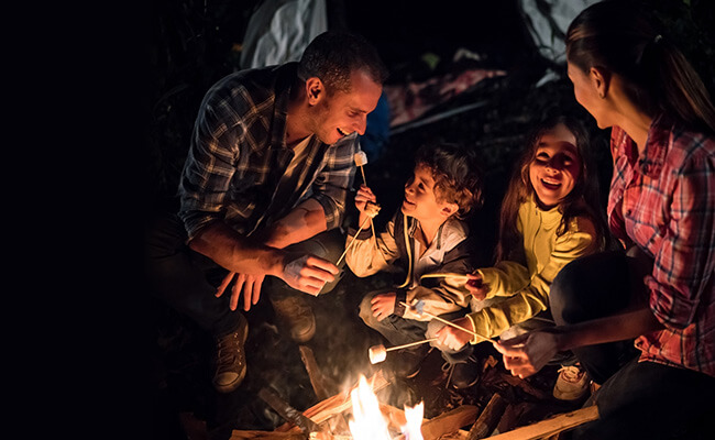 Een gezin met een vader, moeder en twee kinderen bij een open haard, 's avonds, marshmallows roosteren